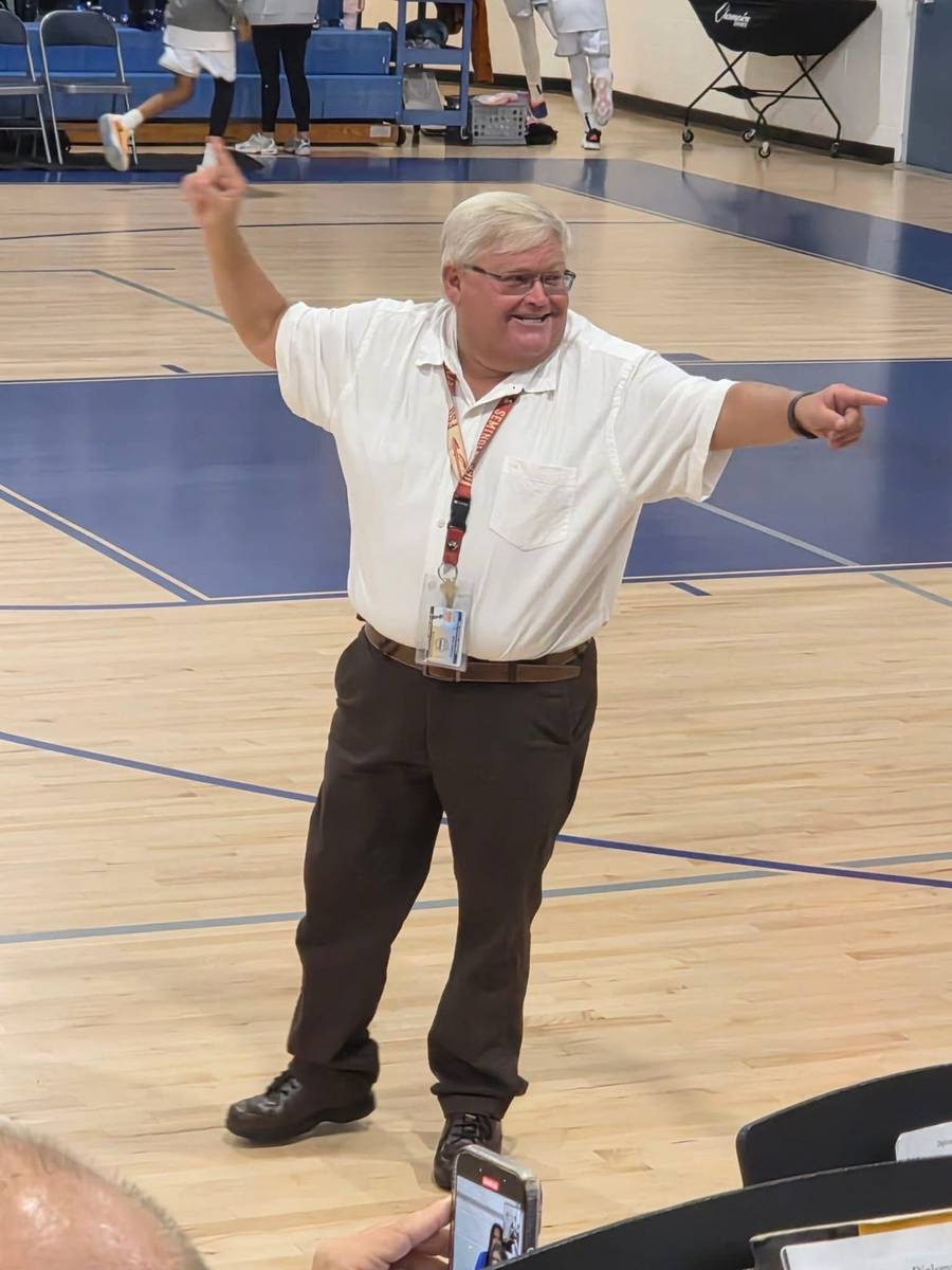 Mark Dahlberg conducting student musicians in a school gymnasium in Lee County, Florida, arms outstretched in direction